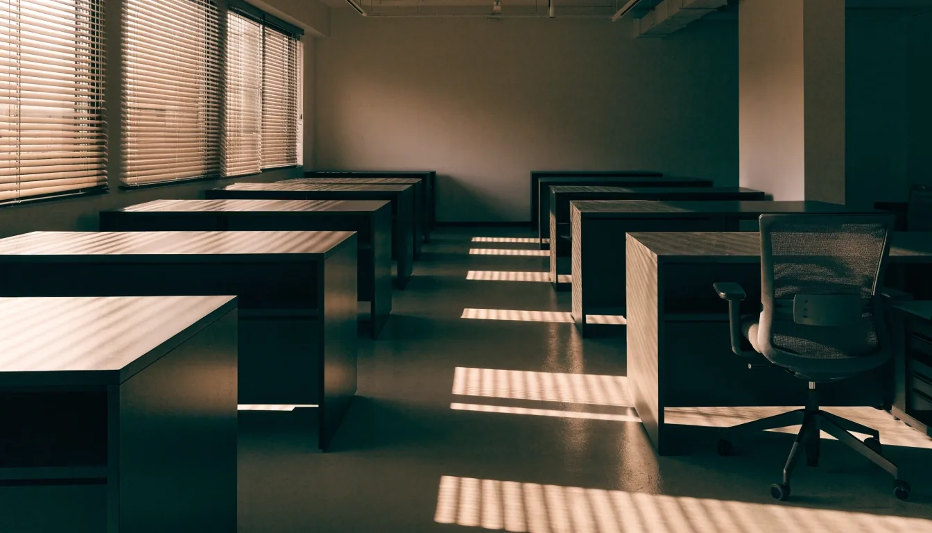 An empty payroll office at morning with warm light striping the floor between rows of desks